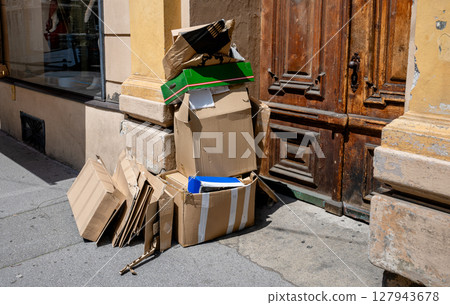 Pile of used cardboard boxes left on the street near old wooden door 127943678
