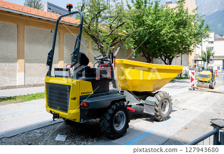 Yellow construction dumper truck parked on urban road during street work Yellow construction dumper truck parked on urban road during street work 127943680