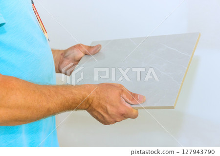 Someone is carefully holding gray tile, ready to be used in home renovation project during works day. Someone is carefully holding gray tile, ready to be used in home renovation project during works day. 127943790