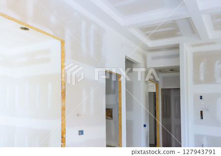 Freshly installed drywall is being prepared in modern home interior with unfinished surfaces open doorways. 127943791