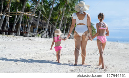 Rear view of mom walking with daughters on tropical beach holding hands 127944561