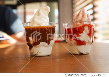 There are two plastic cups containing delicious strawberry and caramel ice cream side by side. There are two plastic cups containing delicious strawberry and caramel ice cream side by side. 127945198