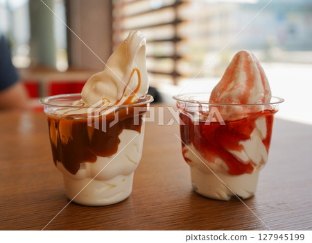 Two cups made of plastic hold creamy strawberry and caramel ice cream, ready to be enjoyed. 127945199