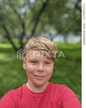 An eleven-year-old guy in a red T-shirt takes a selfie on the street 127945211