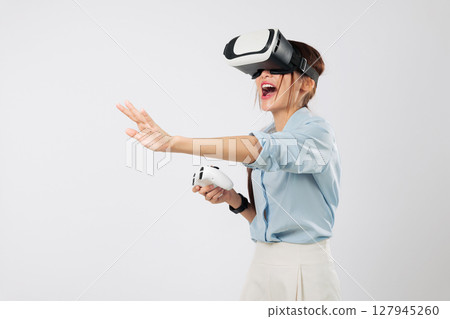 VR game experience as young Asian woman touches imaginary digital VR game interface with palm while playing using controller in virtual world. isolated studio white background 127945260