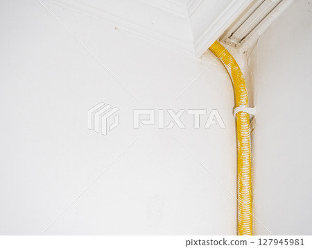 Spiral pipe for the cable from a home refrigerator. Yellow pipe in the apartment. Elastic pipe. On the wall to the freezer. 127945981