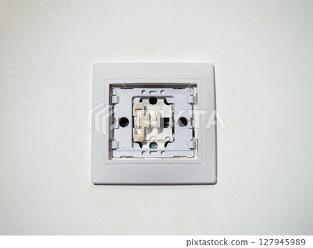 Broken electrical switch on the wall. Switch without button. Disassembled device. White wall with electric light switch. Appliances. 127945989