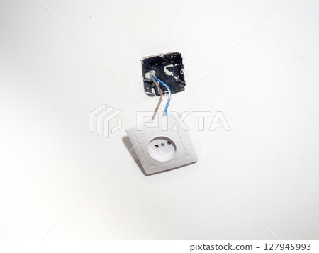 Broken electrical socket on the wall. Disassembled device. White wall with a socket pulled out of the wall. Life threatening. Broken electrical equipment concept. Appliances. Wires out. 127945993