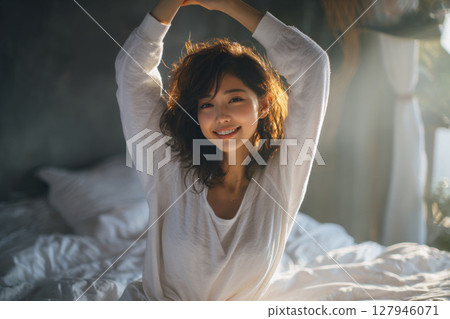 一位年輕女子在床上微笑，清晨的陽光照進來，醒來 127946071