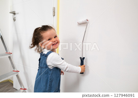 Smilling child with curly hair painting a white wall in the apartment . Smilling child with curly hair painting a white wall in the apartment . 127946091