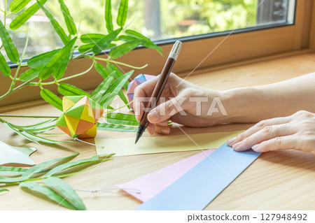 Woman's hand writing a wish on a Tanabata paper strip Woman's hand writing a wish on a Tanabata paper strip 127948492