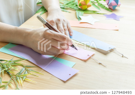 Woman's hand writing a wish on a Tanabata paper strip 127948493