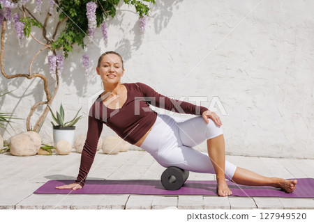 Athletic woman demonstrates foam massage roller technique for thigh and hip recovery on yoga mat in bright modern studio Athletic woman demonstrates foam massage roller technique for thigh and hip recovery on yoga mat in bright modern studio 127949520