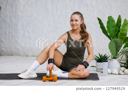 Young athletic woman relaxing after a modern workout at home with dumbbell healthy lifestyle and positive energy Young athletic woman relaxing after a modern workout at home with dumbbell healthy lifestyle and positive energy 127949529