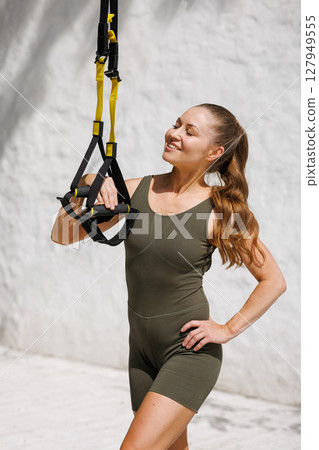 Confident fit woman holding suspension straps outdoors promoting healthy lifestyle and functional bodyweight training 127949555