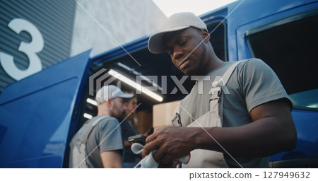 Loader Using Smartphone, Looking at Camera with Surprised Look. Diverse Workers Loading Delivery Truck Loader Using Smartphone, Looking at Camera with Surprised Look. Diverse Workers Loading Delivery Truck 127949632
