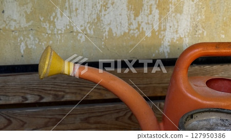 A worn red faucet and plastic garden hose hang on a faded yellow wall, illustrating rural outdoor utility. A worn red faucet and plastic garden hose hang on a faded yellow wall, illustrating rural outdoor utility. 127950386