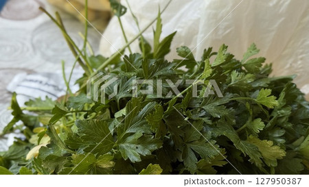 Bunch of vibrant green parsley leaves placed on a white patterned tablecloth, ready for cooking or kitchen prep. 127950387