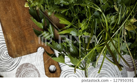 Cut parsley stems with a kitchen knife resting on a wooden chopping board, indicating food preparation in progress. 127950391