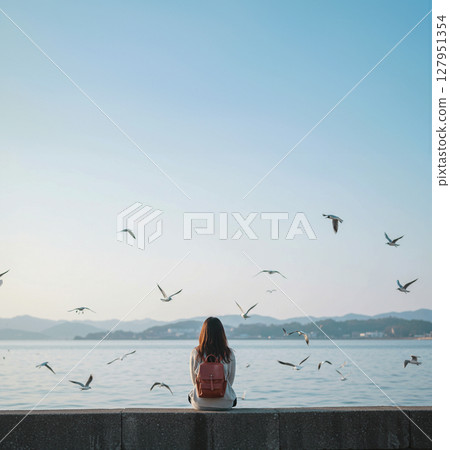 Back view of a girl sitting on a dike and watching seabirds Back view of a girl sitting on a dike and watching seabirds 127951354