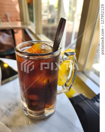 Lo Han Kuo or Monk Fruit Drink, an iced herbal beverage with a dark amber hue and a spoon, set by a sunlit window. Lo Han Kuo or Monk Fruit Drink, an iced herbal beverage with a dark amber hue and a spoon, set by a sunlit window. 127952129
