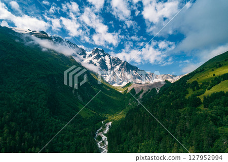Majestic snow-capped Caucasus mountains rise above lush green valleys and a winding river on a sunny day in the wilderness Majestic snow-capped Caucasus mountains rise above lush green valleys and a winding river on a sunny day in the wilderness 127952994