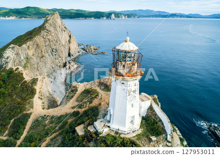 A weathered lighthouse stands on a rugged cliff, overlooking a vast ocean. 127953011