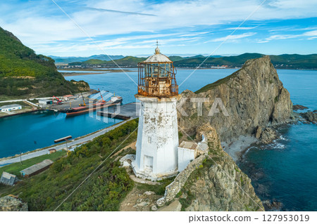 This old lighthouse overlooks a rocky coastline, providing a stunning view of the harbor where ship is moored This old lighthouse overlooks a rocky coastline, providing a stunning view of the harbor where ship is moored 127953019