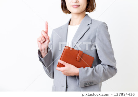 一位身著西裝的中年婦女拿著筆記本,食指向上 一位身著西裝的中年婦女拿著筆記本,食指向上 127954436