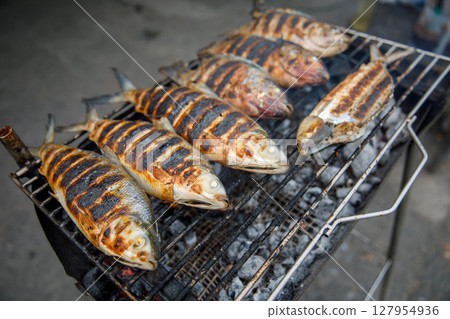 Grilled Fish on Charcoal Grill, Barbecue Seafood Preparation with Burn Marks and Crisp Skin Grilled Fish on Charcoal Grill, Barbecue Seafood Preparation with Burn Marks and Crisp Skin 127954936