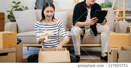 Asian young attractive couple man and woman use tablet and smartphone online shopping furniture decorate house with carton package move in new house. 127955751