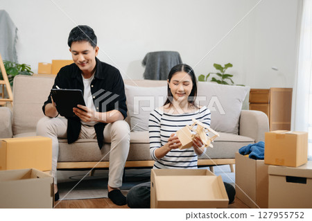Asian young attractive couple man and woman use tablet and smartphone online shopping furniture decorate house with carton package move in new house. Asian young attractive couple man and woman use tablet and smartphone online shopping furniture decorate house with carton package move in new house. 127955752