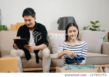 Asian young attractive couple man and woman use tablet and smartphone online shopping furniture decorate house with carton package move in new house. 127955753
