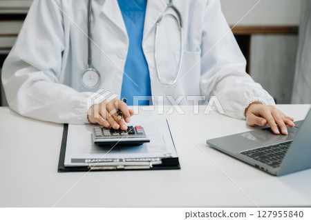 Healthcare costs and fees concept.Hand of smart doctor used a calculator and smartphone, tablet for medical costs at hospital 127955840