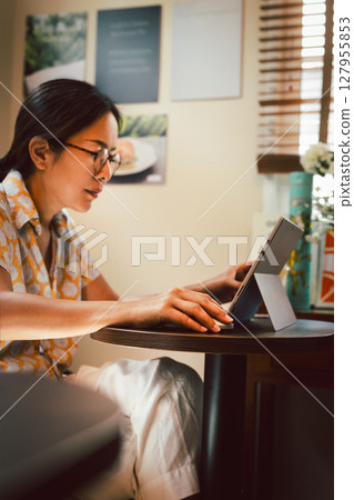 Asian woman working with a laptop sitting at a cafe table. Asian woman working with a laptop sitting at a cafe table. 127955853