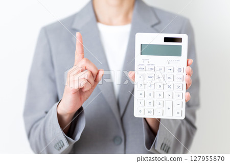 A middle-aged woman in a suit holding a white calculator and pointing her index finger up 127955870