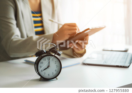 Alarm clock on the desk. Business hand using smartphone, laptop and tablet working in modern office building Alarm clock on the desk. Business hand using smartphone, laptop and tablet working in modern office building 127955880