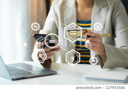 Woman using smart phone for mobile payments online shopping, omni channel, sitting on table, virtual icons graphics interface 127955888
