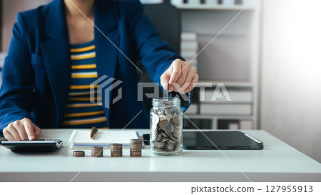 saving money with hand putting coins in jug glass and calculator to calculate budget concept finance and accounting saving money with hand putting coins in jug glass and calculator to calculate budget concept finance and accounting 127955913