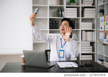 Young Asian business man using laptop and tablet while sitting at her working place. Concentrated at work. 127955954