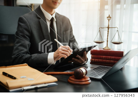 justice and law concept.law theme wooden desk, books, balance. Male judge in a courtroom the gavel,working with digital tablet computer on table justice and law concept.law theme wooden desk, books, balance. Male judge in a courtroom the gavel,working with digital tablet computer on table 127956343