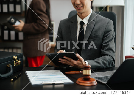justice and law concept.law theme wooden desk, books, balance. Male judge in a courtroom the gavel,working with digital tablet computer on table justice and law concept.law theme wooden desk, books, balance. Male judge in a courtroom the gavel,working with digital tablet computer on table 127956344