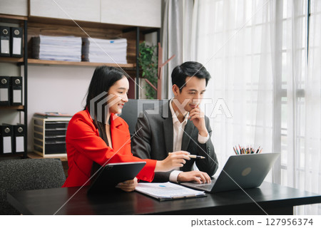 Asian business colleague business presents and explains and using laptop and tablet. Teamwork, financial marketing team,   while sitting in modern office 127956374