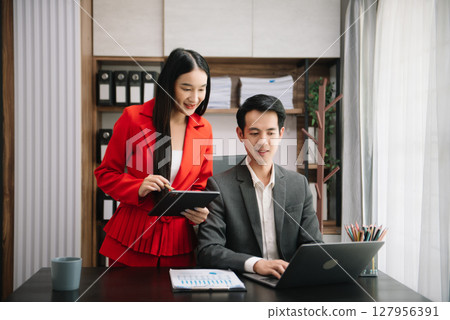 Asian business colleague business presents and explains and using laptop and tablet. Teamwork, financial marketing team, while sitting in modern office Asian business colleague business presents and explains and using laptop and tablet. Teamwork, financial marketing team, while sitting in modern office 127956391