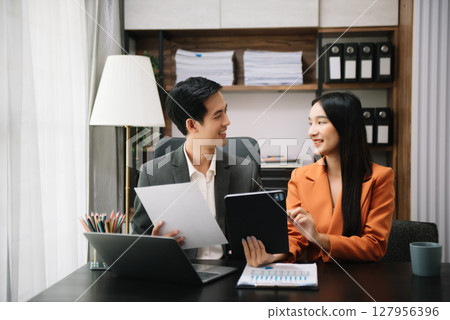 Asian business colleague business presents and explains and using laptop and tablet. Teamwork, financial marketing team, while sitting in modern office Asian business colleague business presents and explains and using laptop and tablet. Teamwork, financial marketing team, while sitting in modern office 127956396