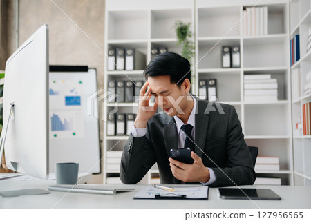 Asian businessman is stressed, bored, and overthinking from working on a tablet at the office. Asian businessman is stressed, bored, and overthinking from working on a tablet at the office. 127956565