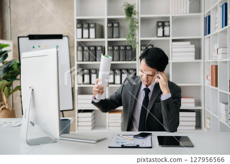 Asian businessman is stressed, bored, and overthinking from working on a tablet at the office. Asian businessman is stressed, bored, and overthinking from working on a tablet at the office. 127956566