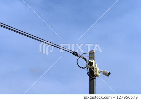 A high-angle surveillance camera mounted on a steel pole contrasts against the backdrop of a clear sky, evoking both vigilance and stillness. A high-angle surveillance camera mounted on a steel pole contrasts against the backdrop of a clear sky, evoking both vigilance and stillness. 127956579