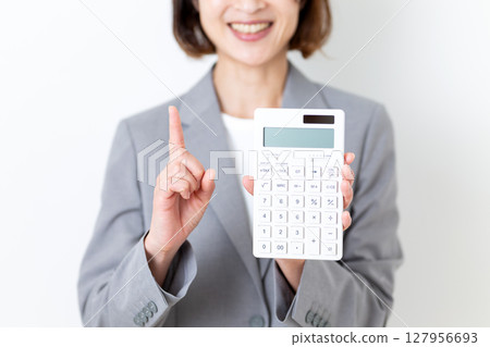 一位身穿西裝的中年女子,手裡拿著一個白色計算器,食指向上 一位身穿西裝的中年女子,手裡拿著一個白色計算器,食指向上 127956693