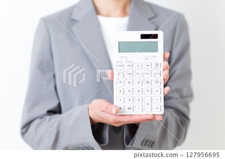一位身穿西裝的中年婦女，手裡拿著一台白色計算器 127956695